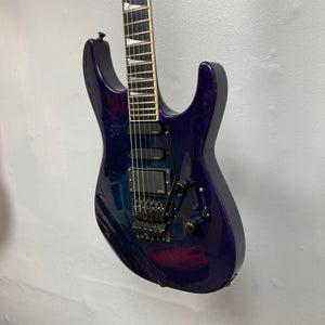 A Jackson 1995 SL1 Soloist Custom Shop electric guitar in Eerie Dess Swirl, featuring a glossy purple finish, three pickups, a tremolo bridge, and black knobs is hanging against a white wall.