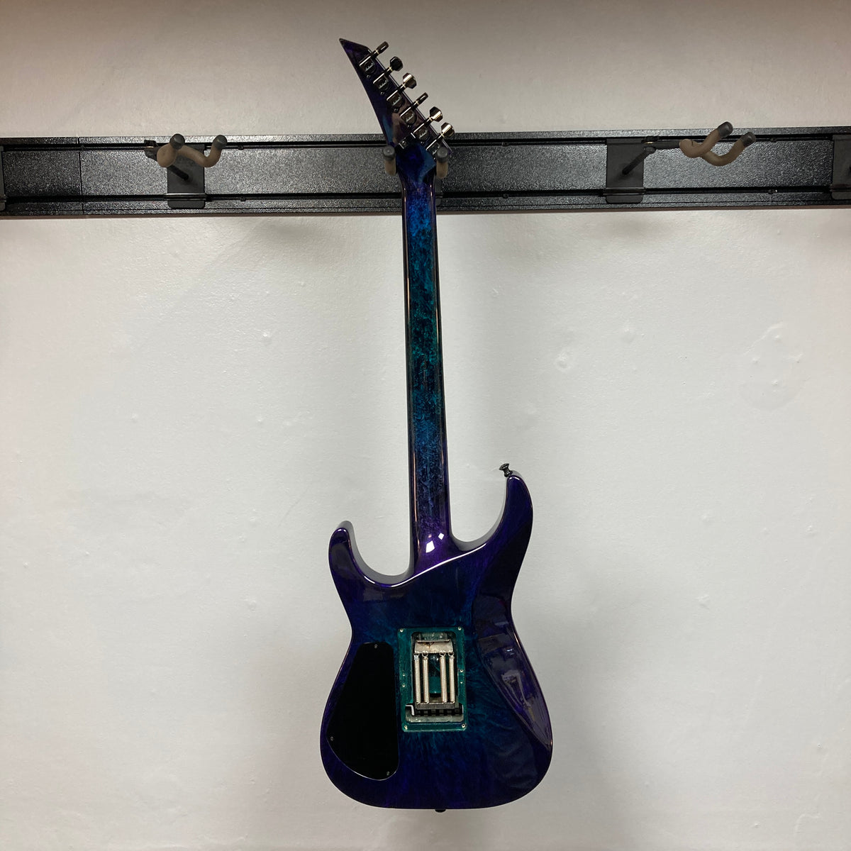 A 1995 Jackson SL1 Soloist Custom Shop electric guitar in Eerie Dess Swirl finish, currently without strings or pickups, is displayed on a black wall mount against a white background, highlighting its premium craftsmanship from Jackson’s USA Custom Shop.