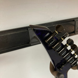 Close-up of the headstock of a Jackson 1995 SL1 Soloist Custom Shop Eerie Dess Swirl electric guitar, featuring black tuning pegs, mounted on a wall hanger against a white wall.