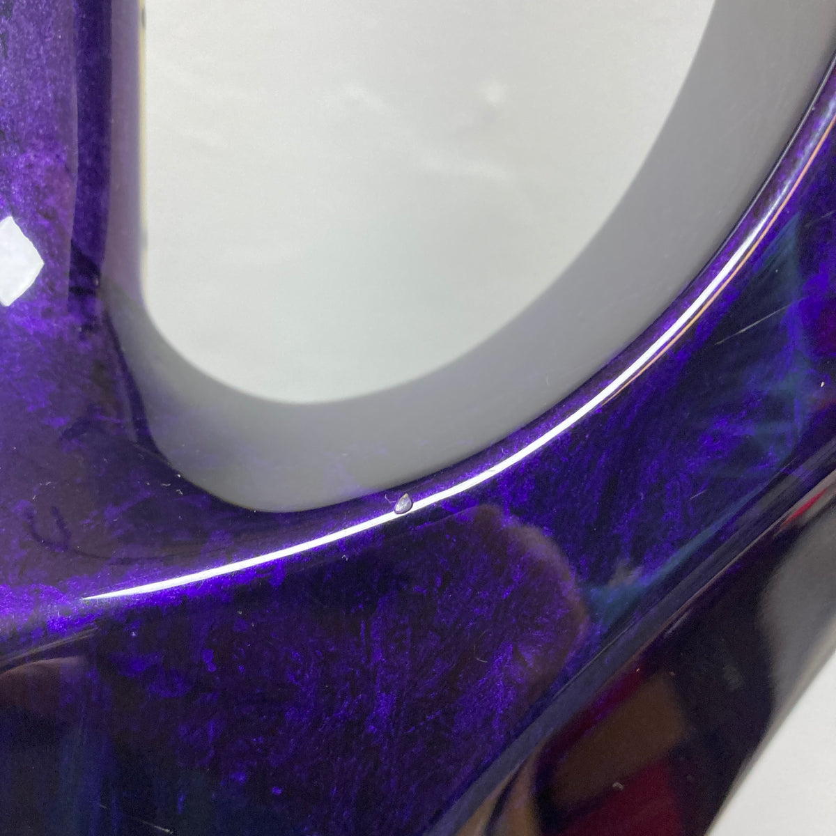 Close-up of a glossy, dark purple surface with a small chip along the curved edge, reflecting light and surrounding colors—reminiscent of the striking Eerie Dess Swirl finish featured on the 1995 Jackson SL1 Soloist Custom Shop, complete with case.