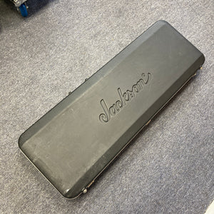 A black Jackson hard guitar case, featuring the “Jackson” logo and made for the 1995 Jackson SL1 Soloist Custom Shop Eerie Dess Swirl w/Case, is lying closed on a gray carpeted floor.