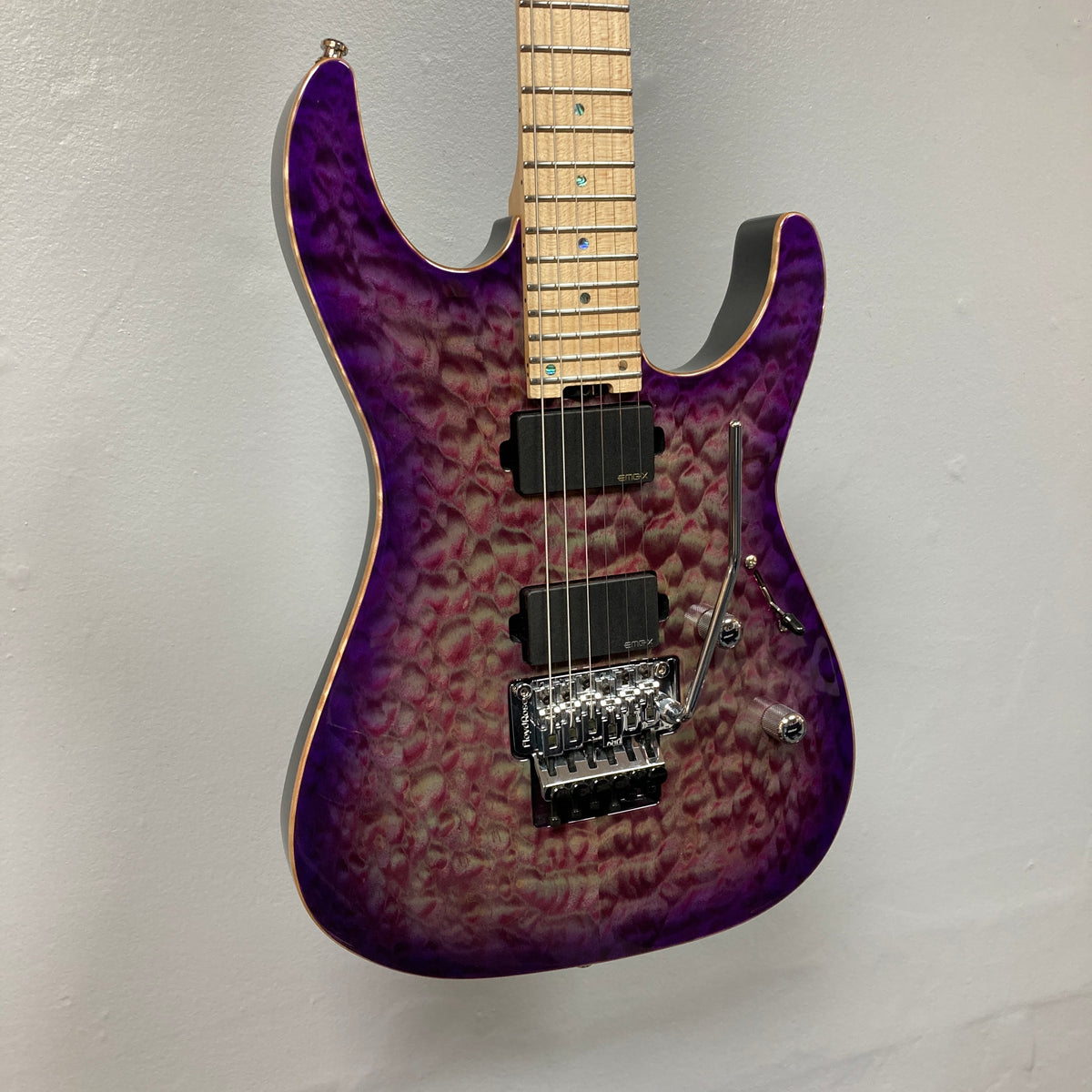 The ESP 2019 USA M-II Purple Haze Burst electric guitar features a breathtaking quilted maple top finished in Purple Haze Burst, a maple neck, dual humbucker pickups, and a Floyd Rose tremolo system. This American-made ESP model is shown photographed against a plain light-colored wall and comes complete with its case.
