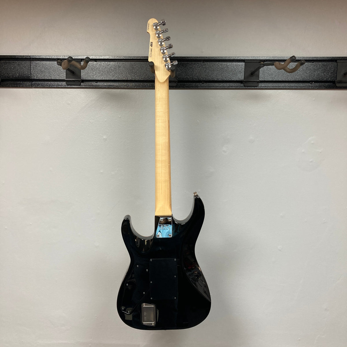 A 2019 ESP USA M-II in Purple Haze Burst, an American-made electric guitar by ESP, is hanging on a wall-mounted rack, shown from the back with the neck and tuning pegs visible.