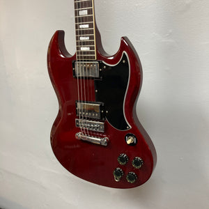 A stunning 1977 Gibson SG Standard Cherry w/Case by Gibson, this red electric guitar showcases a vibrant cherry finish on its mahogany body, featuring a distinctive double-cutaway design, two humbucker pickups, four control knobs, and a sleek black pickguard—an unmistakable classic from the iconic Kalamazoo era.