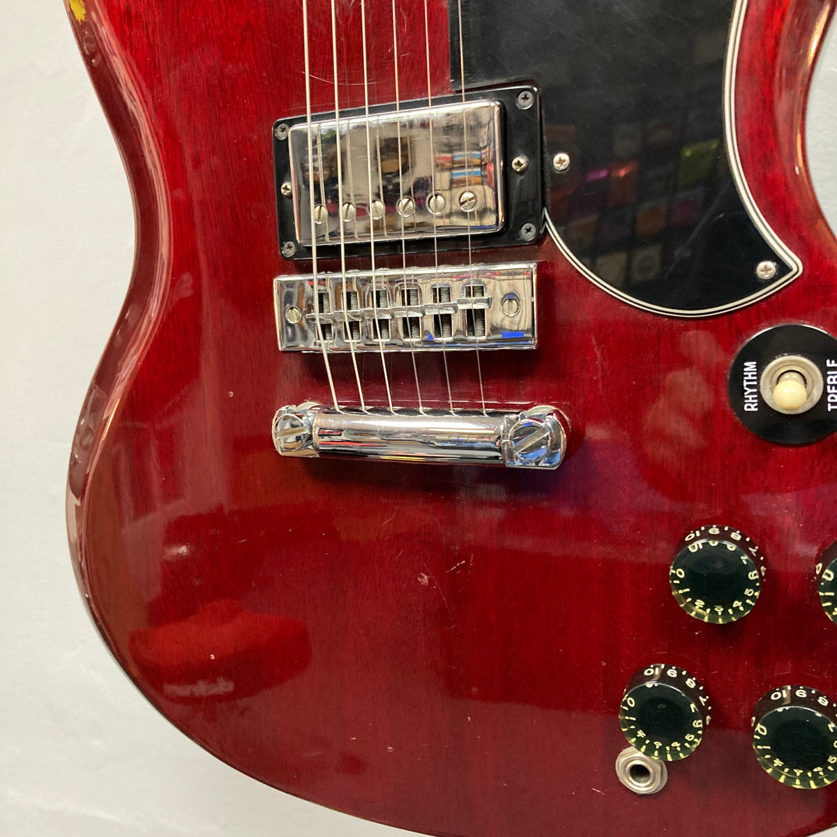 Close-up of a 1977 Gibson SG Standard Cherry electric guitar by Gibson, featuring its rich mahogany body, dual pickups, four control knobs, selector switch, and portions of the bridge and pickguard—a classic instrument from the renowned Gibson Kalamazoo era.