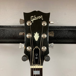 A close-up of the Gibson headstock showcases six tuning pegs, the iconic Gibson logo, and a distinctive inlay above a truss rod cover marked “S-G.” This 1977 Gibson SG Standard Cherry w/Case, made during the legendary Kalamazoo era, displays classic design elements that beautifully complement its sleek mahogany construction.