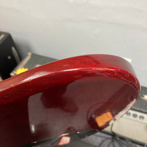 Close-up of the body of a 1977 Gibson SG Standard Cherry w/Case by Gibson, showing visible scratches and finish wear along the edge—characteristics of its vintage mahogany construction from the renowned Kalamazoo era; amplifiers and cases appear blurred in the background.