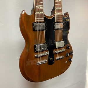 A 1978 Gibson EDS-1275 Double Neck electric guitar in a walnut finish, featuring a black pickguard, chrome hardware, and multiple control knobs, is displayed hanging on a white wall.