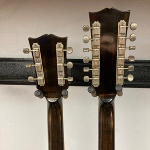 Two stringed instrument headstocks with metal tuning pegs are shown from the back, side by side, mounted on a black wall rack against a white background—one of them is the Gibson 1978 EDS-1275 Double Neck Walnut w/Case.
