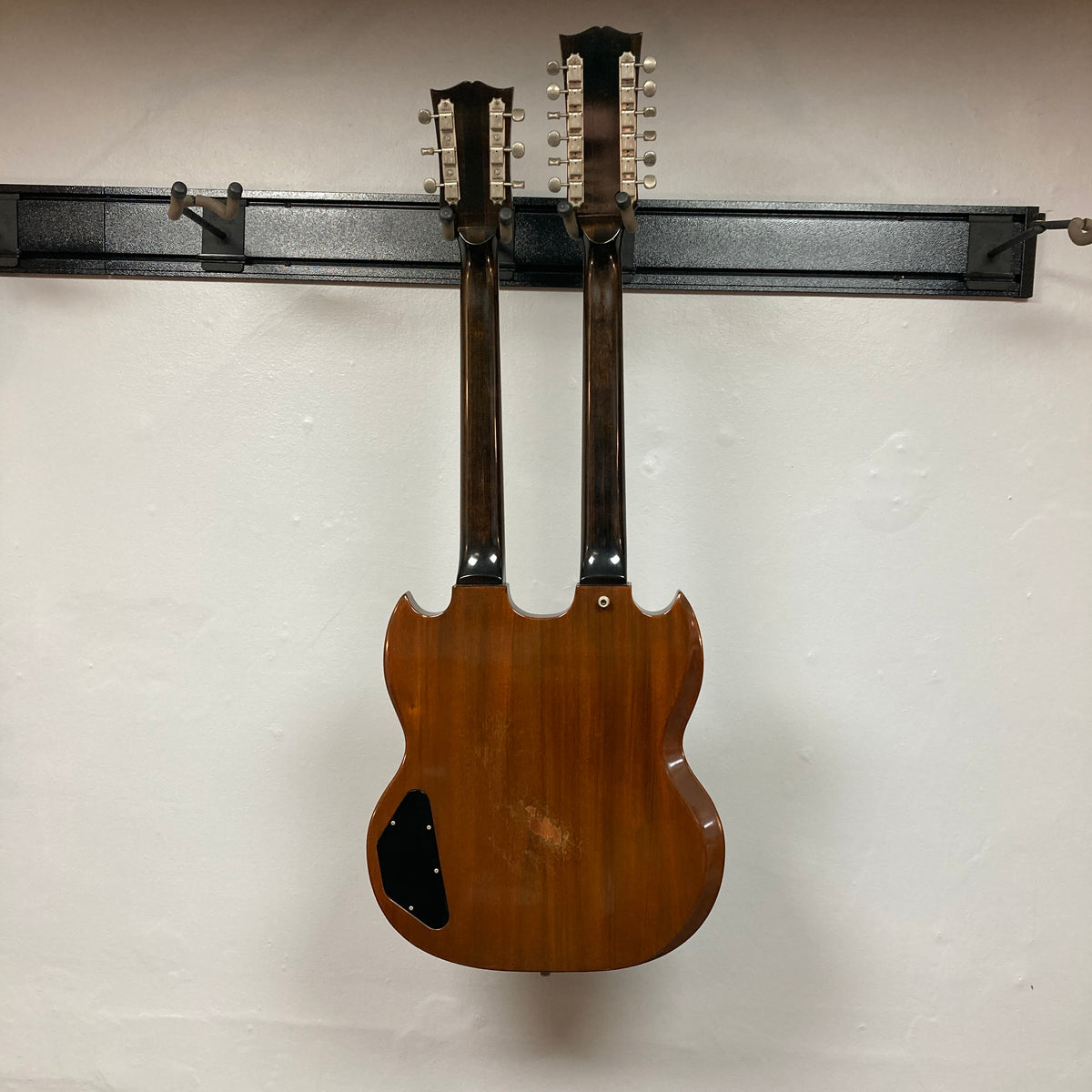 A 1978 Gibson EDS-1275 Double Neck Walnut guitar by Gibson hangs on a wall-mounted rack against a plain white background.