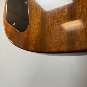 Close-up of the back corner of a Gibson 1978 EDS-1275 Double Neck Walnut guitar body, showcasing a black plastic cover and reflective surface, set against a plain gray background.
