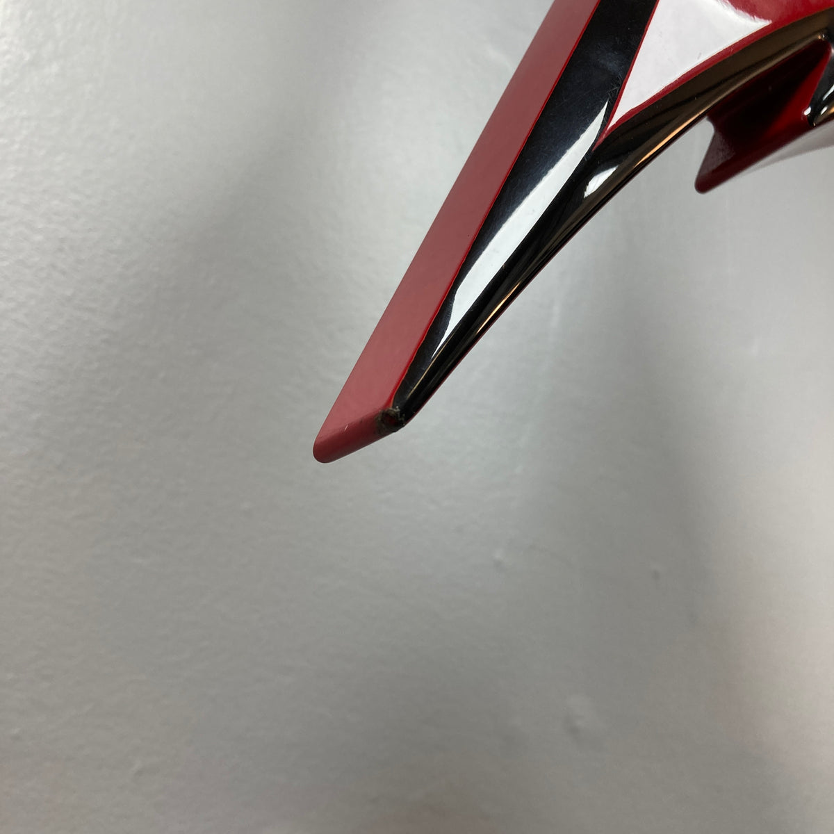 Close-up of a shiny red and black Jackson Phil Demmel Demmelition King V electric guitar with a pointed edge, set against a plain light gray background, showcasing its iconic Floyd Rose tremolo system.