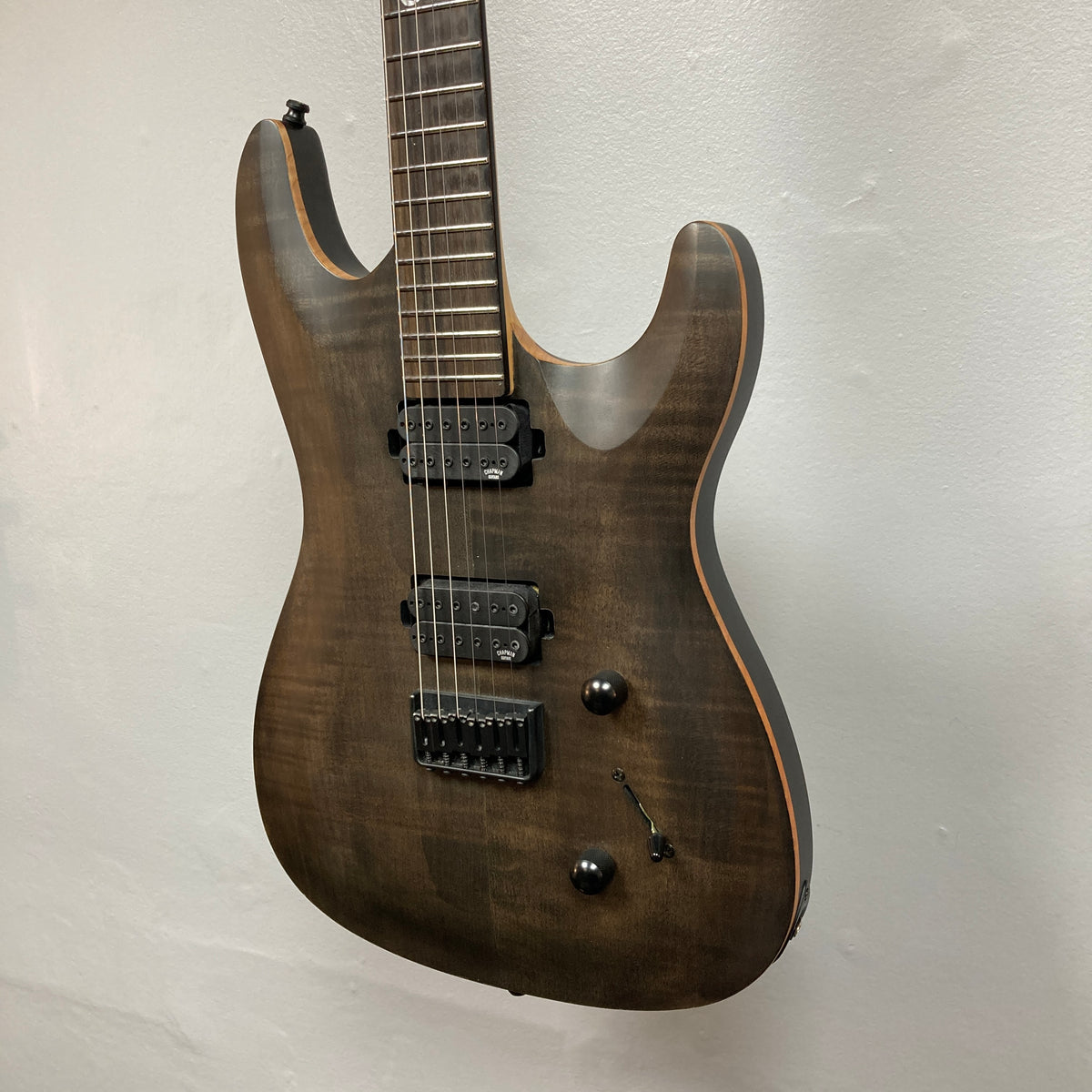 Chapman ML1 Pro Modern Lunar electric guitar by Chapman, featuring a dark wood finish, dual humbucker pickups, two control knobs, and a selector switch, hangs against a plain light-colored wall. This modern guitar also offers a sleek 24-fret fingerboard for extended playability, and comes with a case.