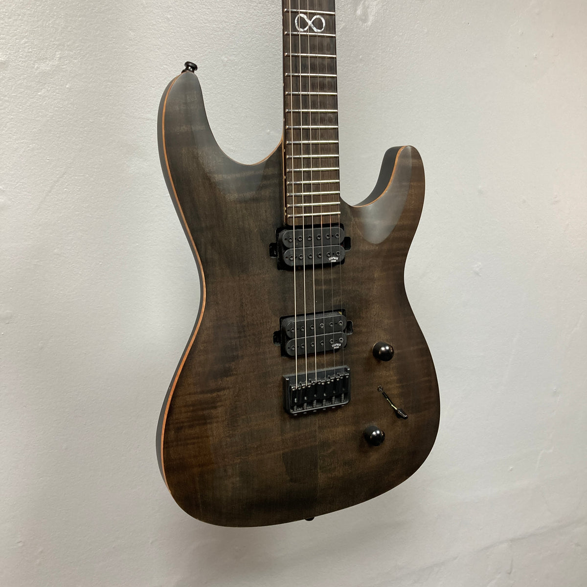 The Chapman ML1 Pro Modern Lunar electric guitar by Chapman, featuring a dark wood finish, dual humbucker pickups, two control knobs, a fixed bridge, and a sleek 24-fret neck, is displayed hanging against a plain white wall.