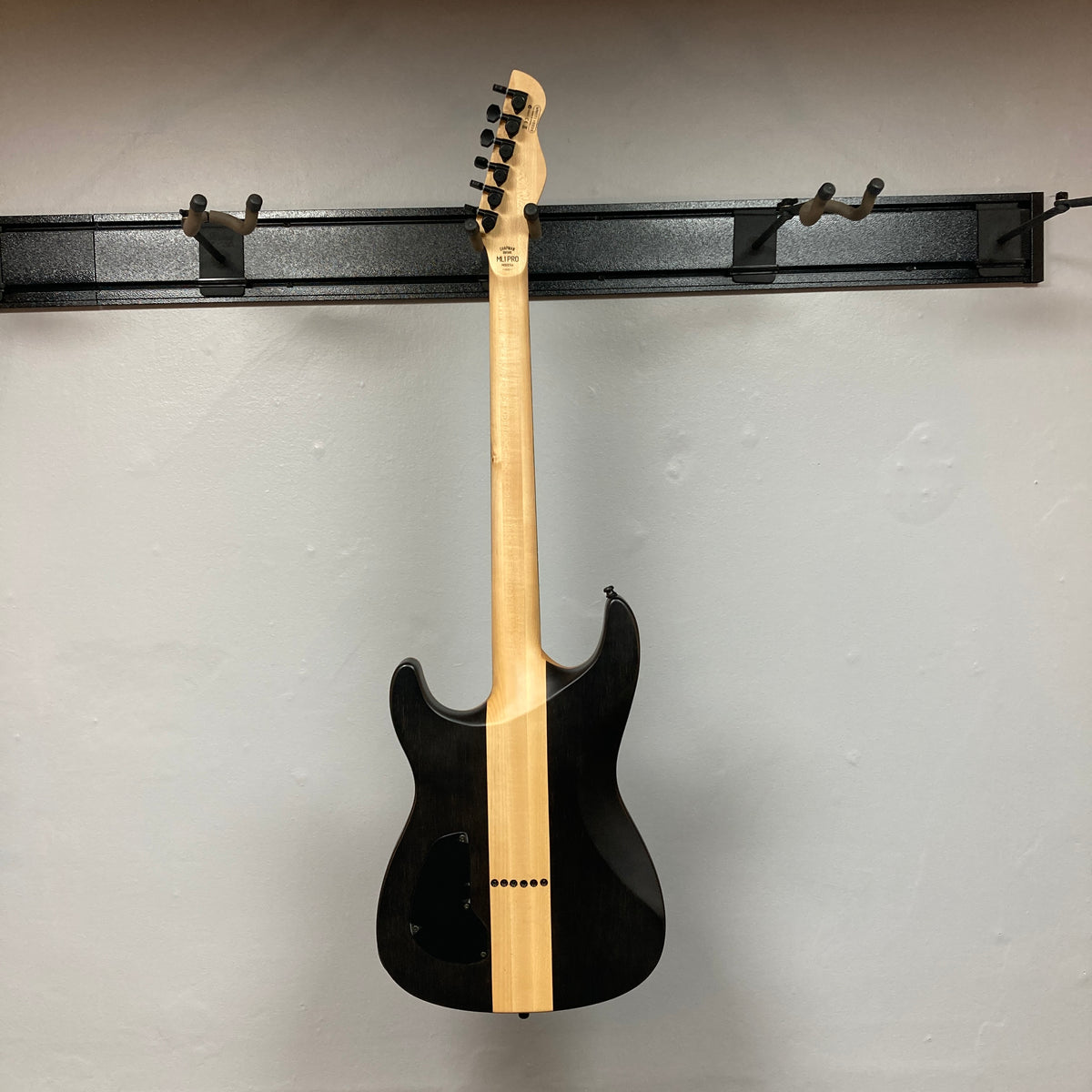 A Chapman ML1 Pro Modern Lunar electric guitar with 24 frets is displayed on a wall-mounted rack, shown from the back with its neck and headstock visible.