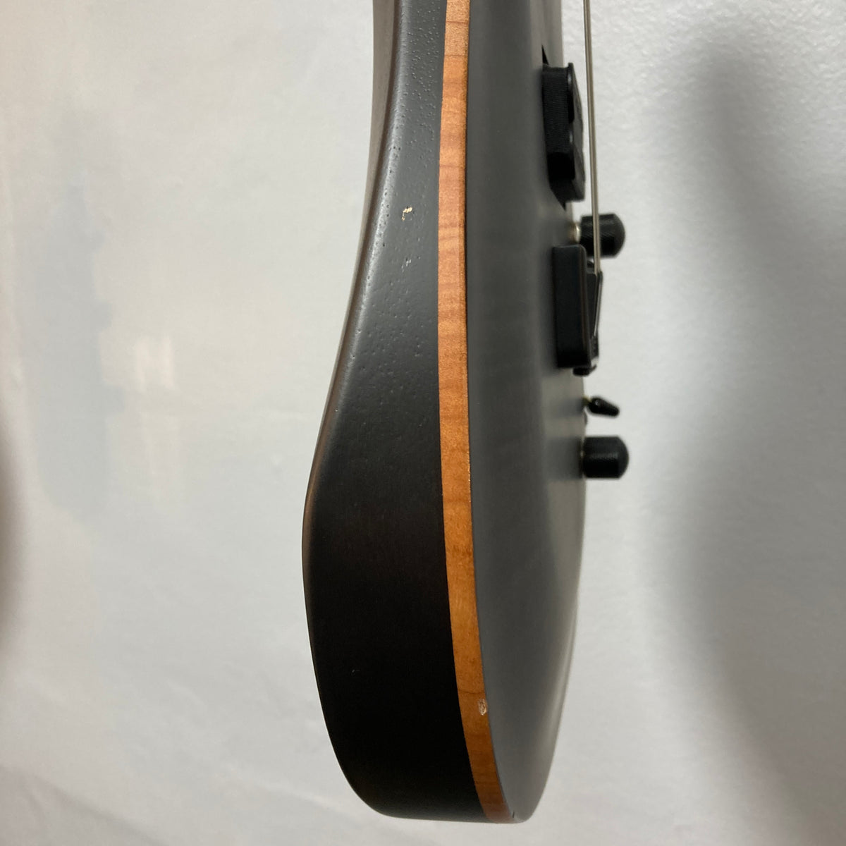 Side view of the Chapman ML1 Pro Modern Lunar electric guitar by Chapman, showcasing its natural wood edge, 24-fret neck, dual humbucker pickups, and black control knobs—all set against a light-colored wall.