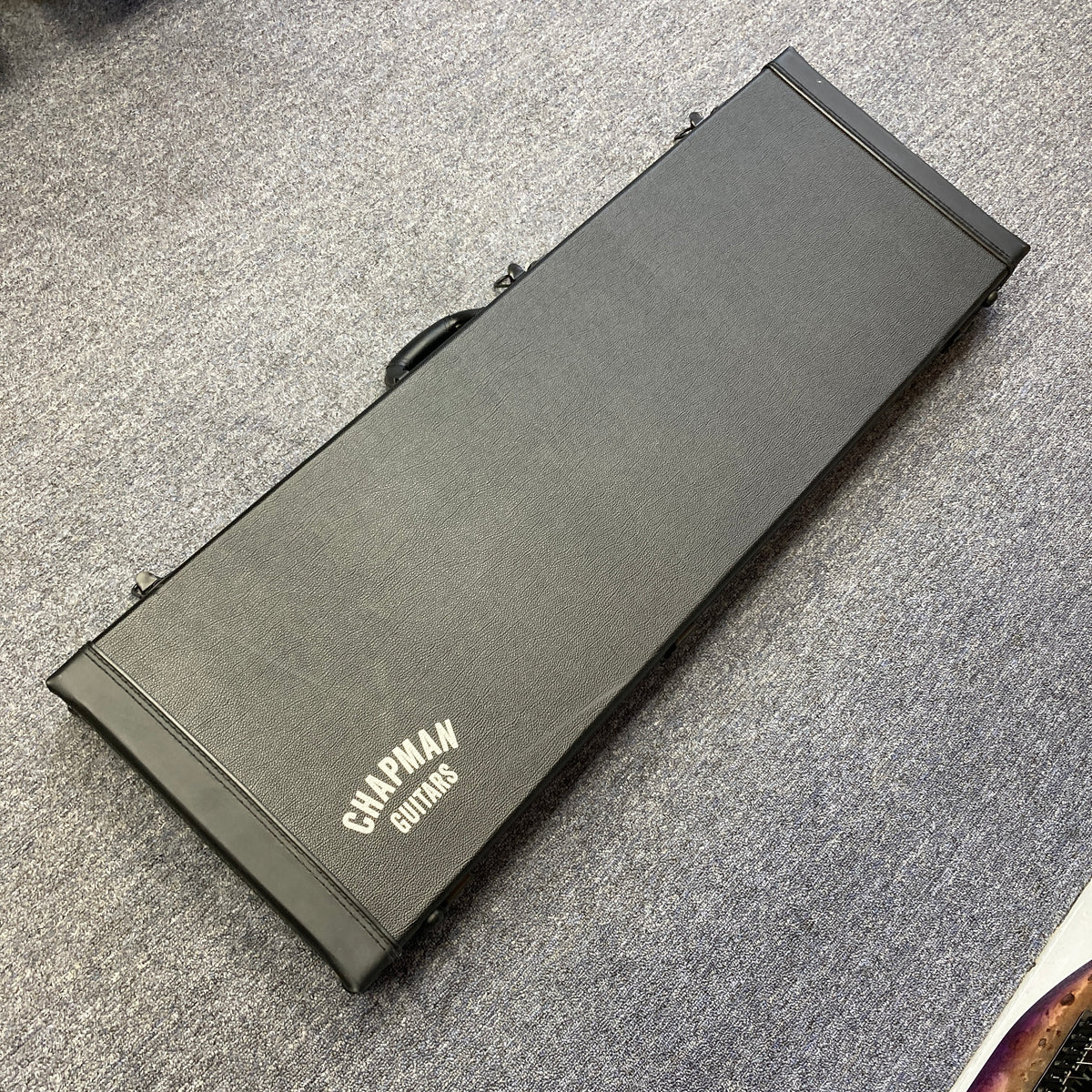 A Chapman ML1 Pro Modern Lunar electric guitar case by Chapman, designed for a dual humbucker, 24-fret model, lies closed on a gray carpeted floor and is photographed from above.