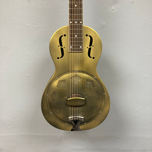 The Republic Parlor Resolian Antique Bronze Resonator w/Case, a brass-bodied six-string guitar featuring f-holes, a single cone, and a metal cover plate, hangs against a plain light gray wall.