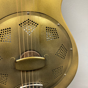 Close-up of the Republic Parlor Resolian Antique Bronze Resonator by Republic, featuring its metallic body with sound holes, metal cover plate, and guitar strings set against a plain background. The single cone design and antique bronze finish enhance its vintage character.