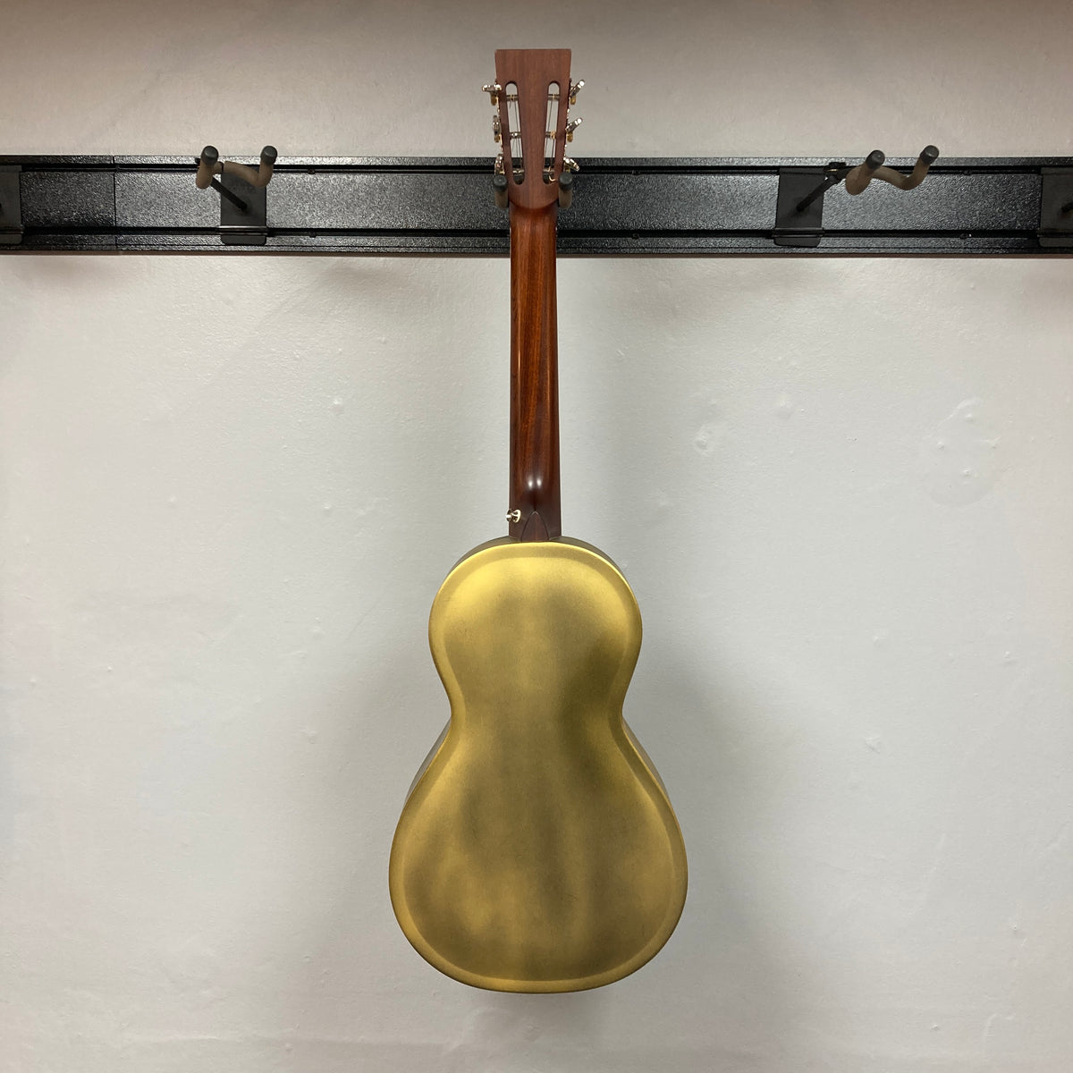 Back view of the Republic Parlor Resolian Antique Bronze Resonator w/Case by Republic, featuring a single cone design, displayed on a wall-mounted black guitar rack against a white wall.