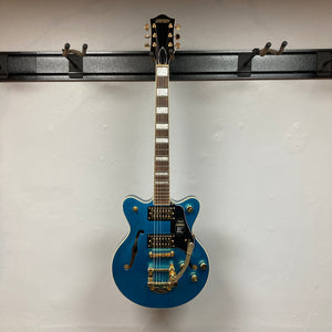 A Gretsch G2655TG Streamliner Riviera Blue Refurb semi-hollow electric guitar with gold hardware hangs on a wall-mounted rack against a white background, showcasing its stylish Broad’Tron BT 3S pickups.