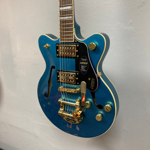 A Gretsch G2655TG Streamliner Riviera Blue Refurb semi-hollow electric guitar with gold hardware, Broad’Tron BT 3S pickups, and a Bigsby vibrato tailpiece hangs on a light-colored wall.
