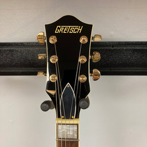 Close-up of a Gretsch G2655TG Streamliner Riviera Blue Refurb guitar headstock with gold tuning pegs and the Gretsch logo, set against a plain wall background.