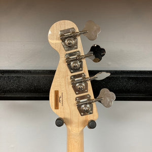 The back of a Squier Paranormal Rascal Bass HH Sherwood Green Refurb headstock, displaying four tuning pegs and a serial number, is mounted on a wall hanger against a white background—highlighting the distinctive short scale bass design from Squier.