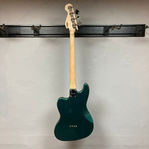 A Squier Paranormal Rascal Bass HH Sherwood Green Refurb hangs on a wall-mounted rack, shown from the back against a plain white wall. This short scale bass by Squier features Fender Designed Wide Range humbuckers, offering both stylish looks and versatile tone.