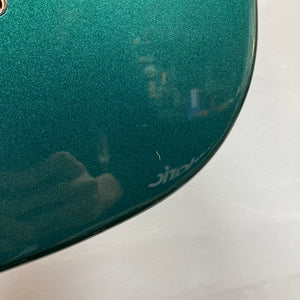 Close-up of the green metallic surface of a Squier Paranormal Rascal Bass HH Sherwood Green Refurb by Squier, highlighting a small white scratch near the edge and faint reflections.