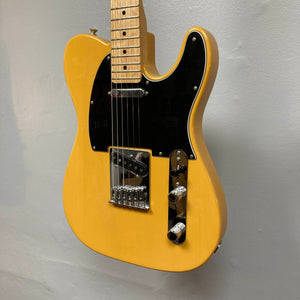 A Fender Player Telecaster 75th Anniversary Butterscotch Used electric guitar, featuring a black pickguard, two pickups, control knobs, and a maple neck, is mounted on a light gray wall.