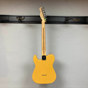 A Fender Player Telecaster 75th Anniversary Butterscotch Used by Fender is displayed hanging on a black wall mount, shown from the back with visible tuning pegs and neck, highlighting its classic maple fingerboard.
