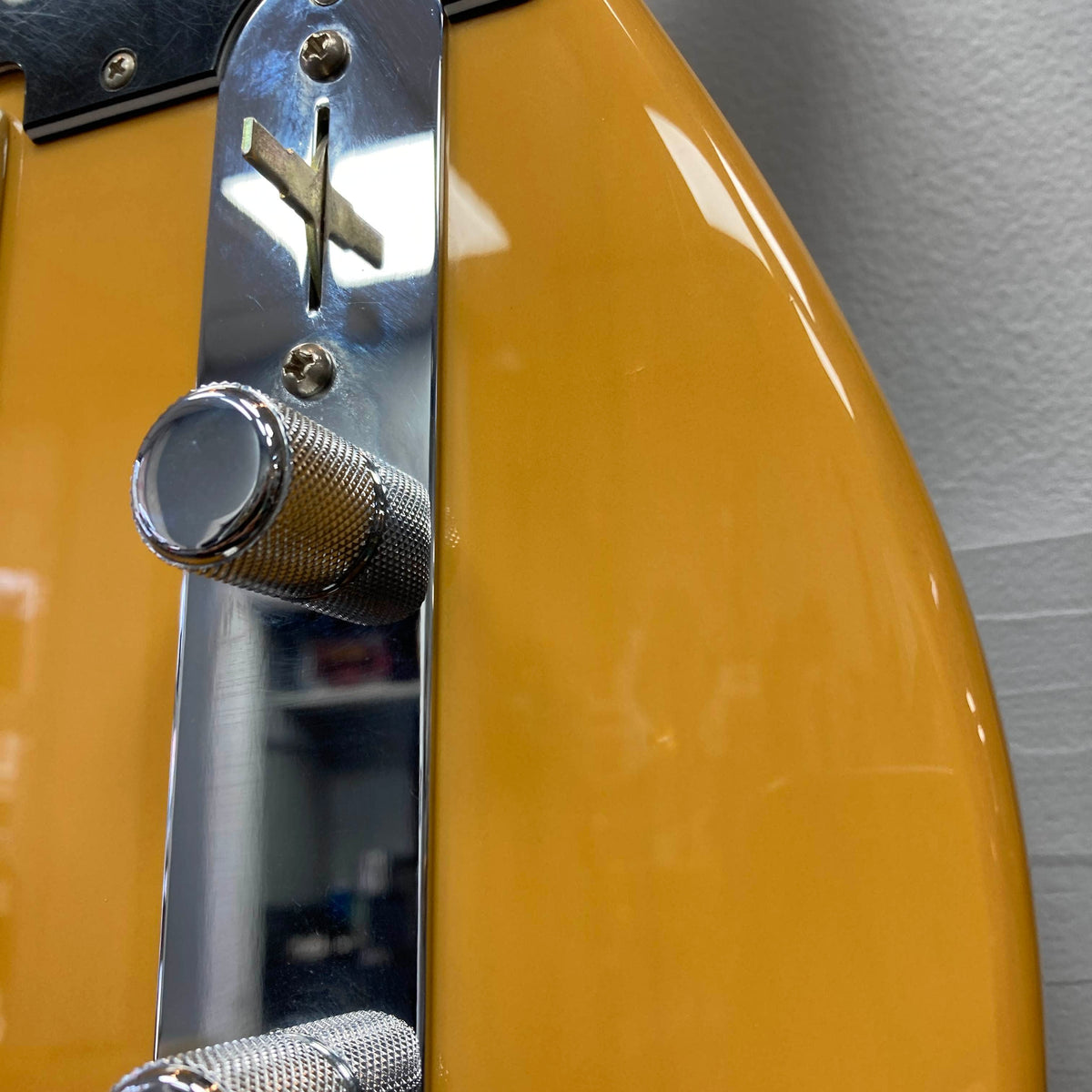 Close-up of a Fender Player Telecaster 75th Anniversary Butterscotch Used electric guitar body by Fender, featuring chrome control knobs, a metal control plate, and part of a wall in the background.