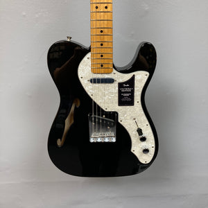 A used Fender Vintera II ’60s Telecaster Thinline in black, featuring a semi-hollow ash body, white pearloid pickguard, maple neck, three control knobs, and vintage-style Tele pickups from Fender, is hanging on a light gray wall.