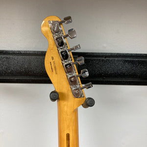 The back of a guitar headstock showing six tuning pegs and part of a black wall-mounted guitar holder, belonging to a Fender Vintera II ’60s Telecaster Thinline Black Used by Fender.