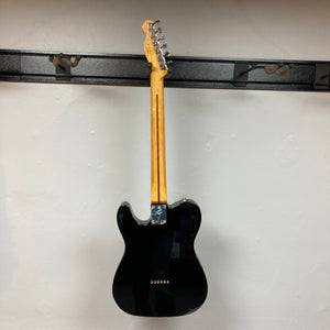 A Fender Vintera II ’60s Telecaster Thinline in black is hanging on a wall with its back facing outward. This eye-catching Fender guitar boasts a semi-hollow ash body and vintage-style Tele pickups, true to the classic ’60s design.