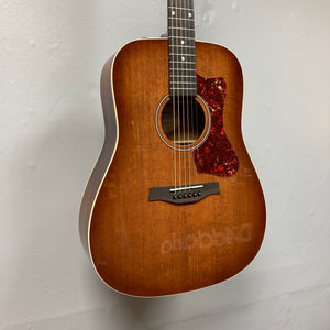 A Godin Century Maho Rustic Burst EQ SF acoustic electric guitar with a tortoiseshell pickguard is hanging on a light-colored wall.