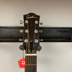 Close-up of the headstock of a Godin Century Maho Rustic Burst EQ SF dreadnought acoustic-electric guitar by Godin, with tuning pegs clearly visible as it hangs on a wall mount. A red tag is attached to one of the tuning pegs, drawing attention to this finely crafted solid wood instrument.