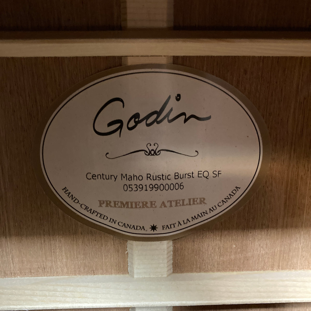 The Godin label inside the body clearly presents the model name “Godin Century Maho Rustic Burst EQ SF,” along with its unique serial number and the phrase “Hand-crafted in Canada” in both English and French. As a dreadnought acoustic electric made from solid wood, this guitar exemplifies Godin’s dedication to quality and expert craftsmanship.