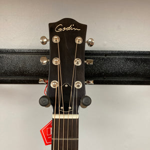 Close-up of the headstock of a Godin Century Maho Rustic Burst EQ SF acoustic guitar by Godin, featuring six tuning pegs, strings, and a red tag hanging from one peg against a plain background. This solid wood guitar blends classic design with modern versatility, making it ideal for both acoustic and electric performance.