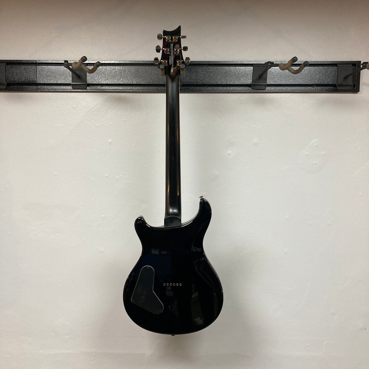 PRS SE Mark Holcomb - Holcomb Blue Burst w/Gigbag Used Consign by PRS hanging on a wall rack, photographed from the back against a plain white wall.