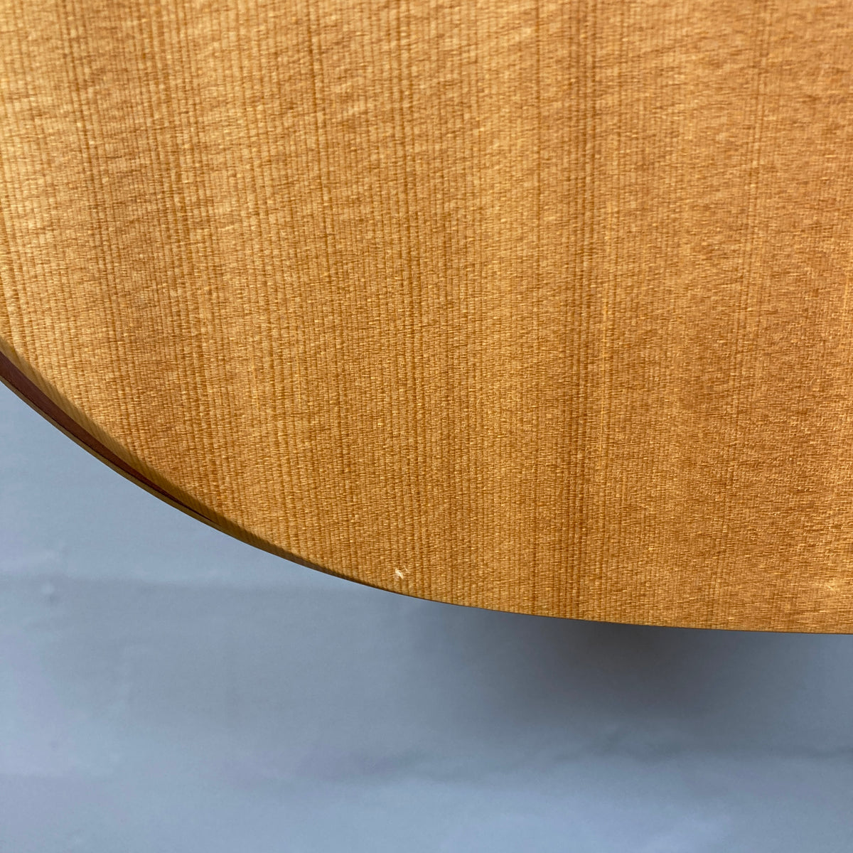 Close-up of the lower edge of a Taylor Academy 10e Acoustic-Electric Guitar w/GigBag, highlighting the wood grain and a small white mark near the bottom.