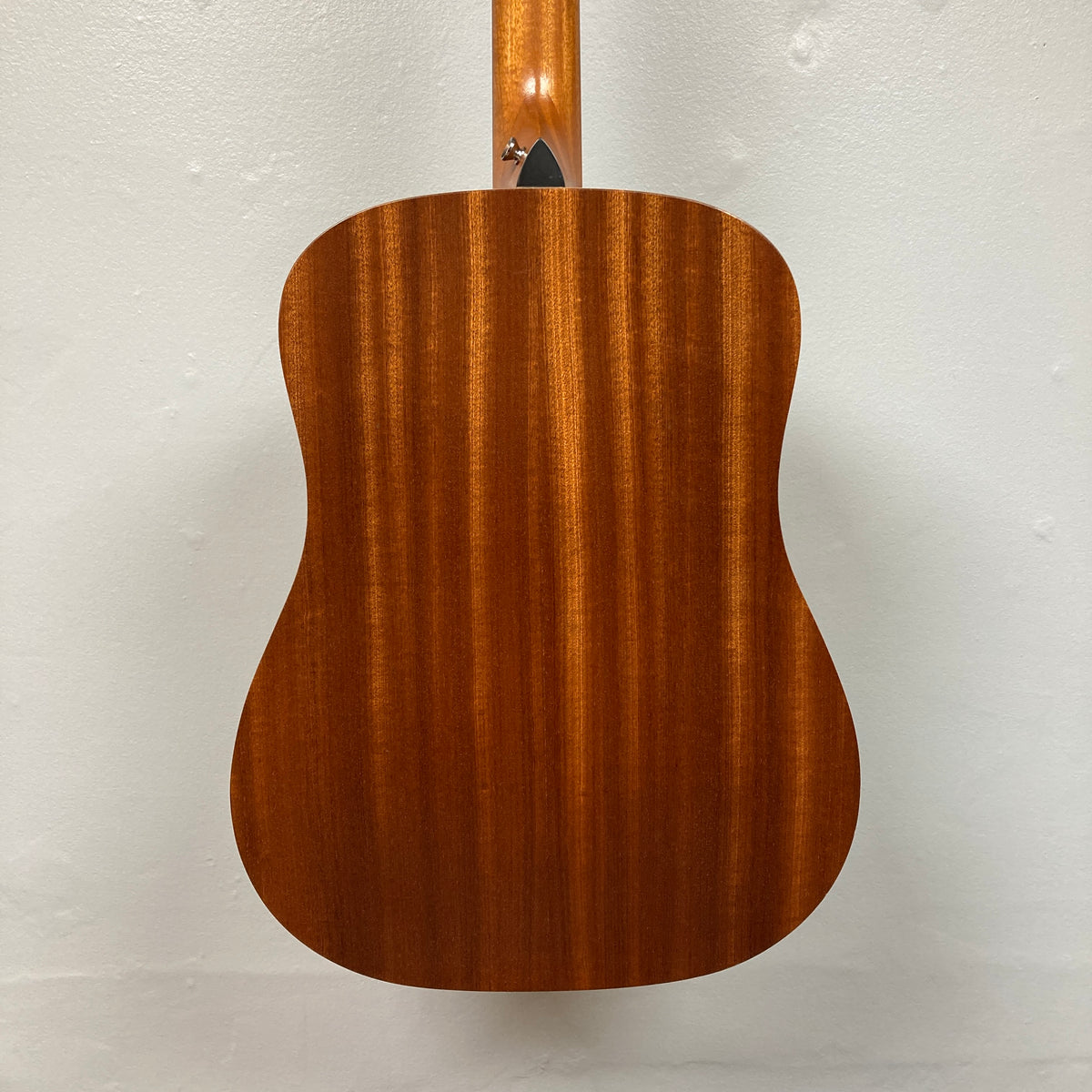 Back view of the Taylor Academy 10e Acoustic-Electric Guitar w/GigBag, natural finish with vertical wood grain patterns against a plain white wall.