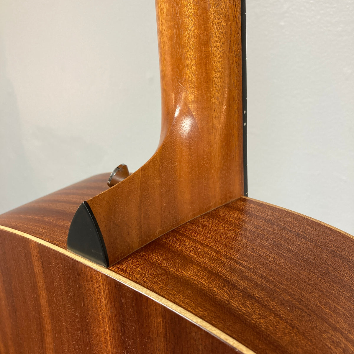 Close-up of a Taylor Academy 10e Acoustic-Electric Guitar w/GigBag neck joint, highlighting the wood grain, smooth finish, and body details against a neutral background.