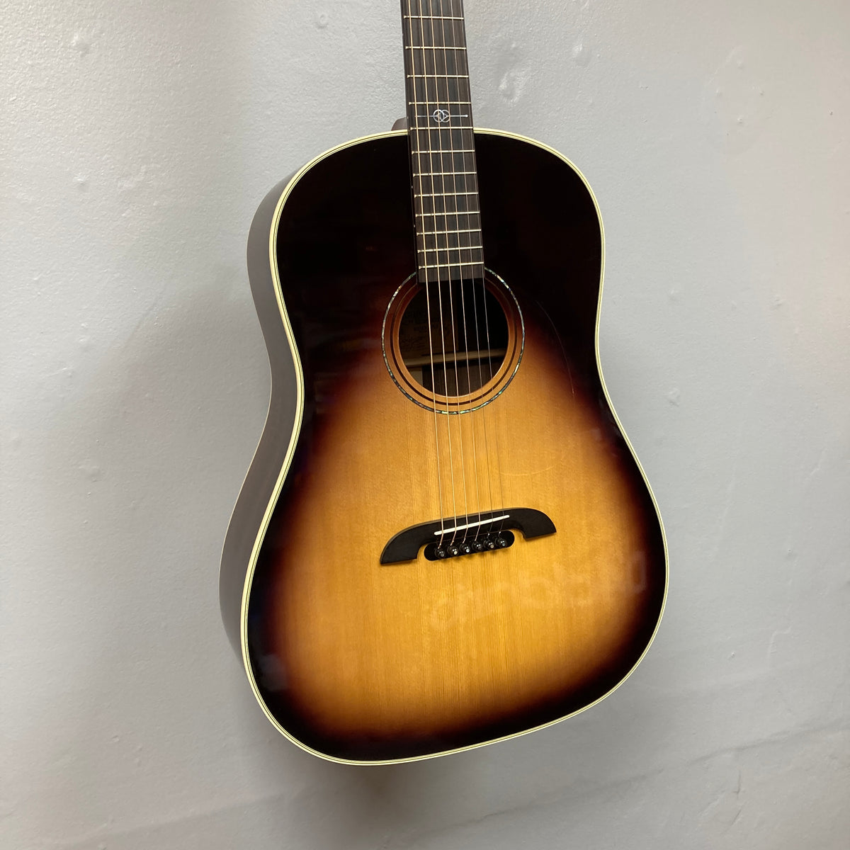 The Alvarez DYMR70SB Yairi Masterworks Acoustic Guitar Sunburst w/Case hangs elegantly on a plain white wall.