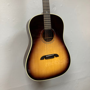 The Alvarez DYMR70SB Yairi Masterworks Acoustic Guitar Sunburst w/Case hangs elegantly on a plain white wall.