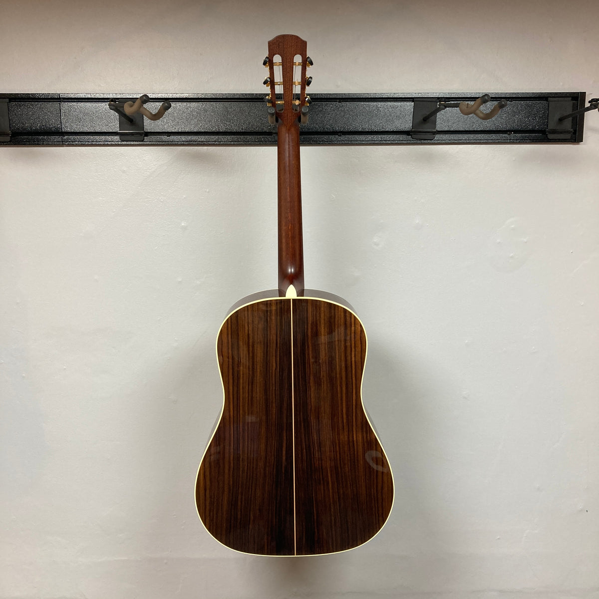 An Alvarez DYMR70SB Yairi Masterworks Acoustic Guitar Sunburst w/Case hangs on a wall-mounted rack against a plain white wall.