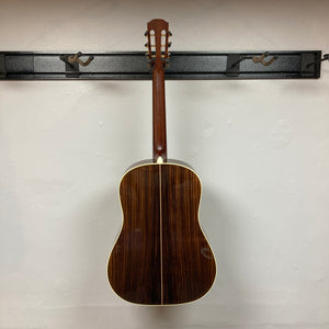 An Alvarez DYMR70SB Yairi Masterworks Acoustic Guitar Sunburst w/Case hangs on a wall-mounted rack against a plain white wall.