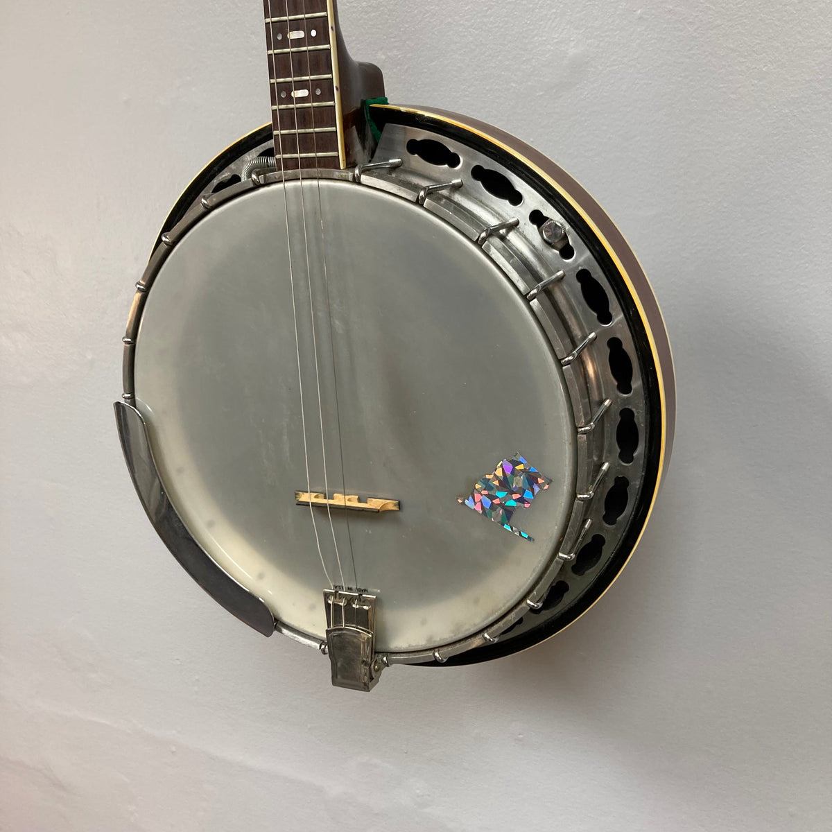 Aria Tenor Banjo 4 String 1970s w/Case hanging on a wall, showcasing its high-quality craftsmanship and chrome-plated hardware.