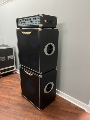 An Ashdown UK Built ABM Bass Rig Full Stack, featuring an EVO II 900 Head with 410T and 115-500 cabinets in flight cases, stands stacked on a wood floor against a light gray wall.